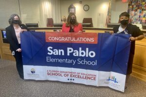 Superintendent, Board Member and school administrator hold banner Congratulations San Pablo Elementary School a Florida Department of Education School of Excellence