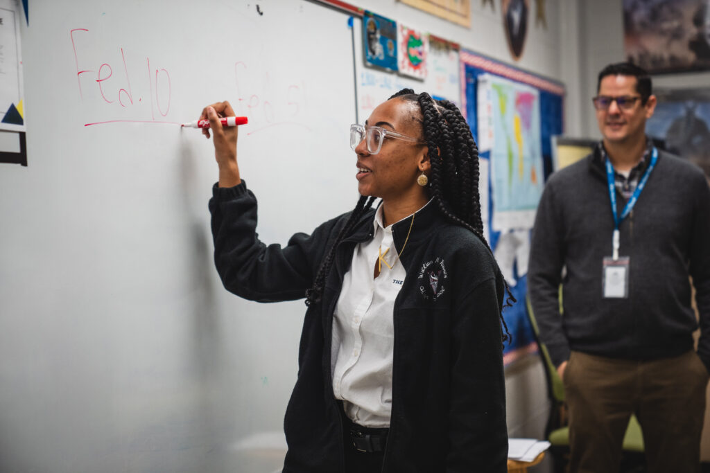 Duval County Public Schools high school student writes on whiteboard as teacher looks on